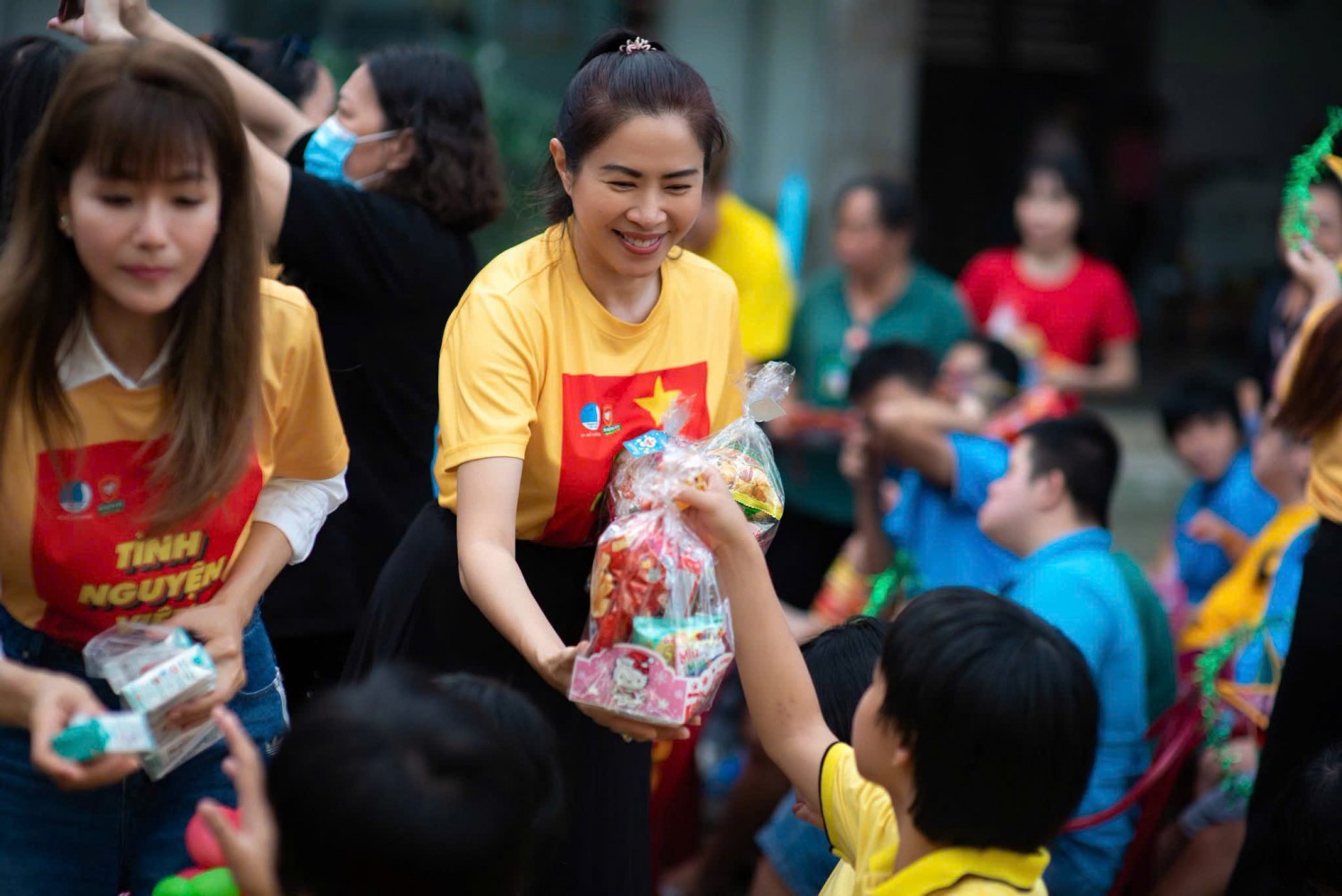 Tình nguyện viên mặc áo thun đồng phục vàng trao quà cho thiếu nhi