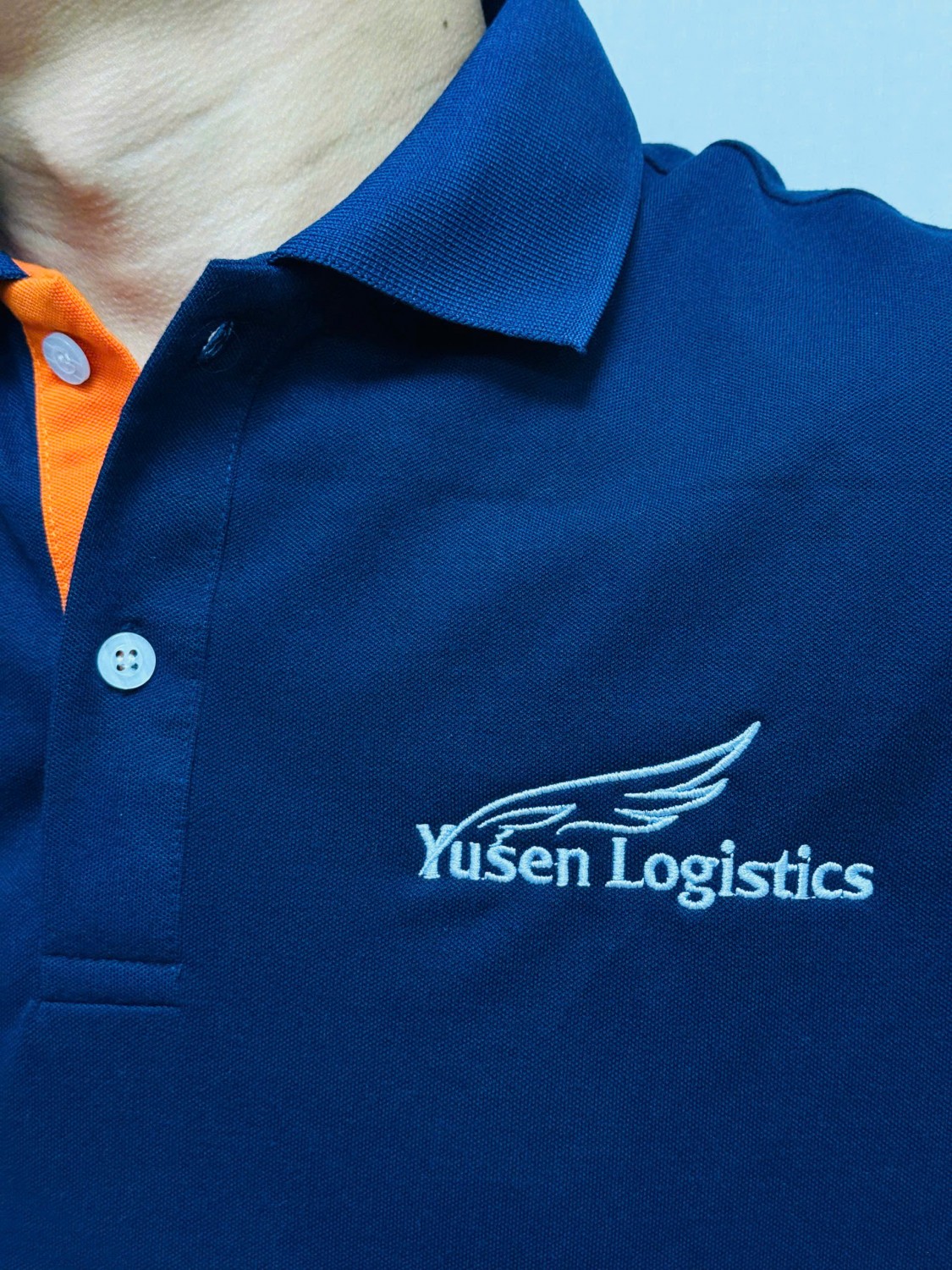 Logo Yusen Logistics thêu trắng trên ngực áo polo xanh đậm.