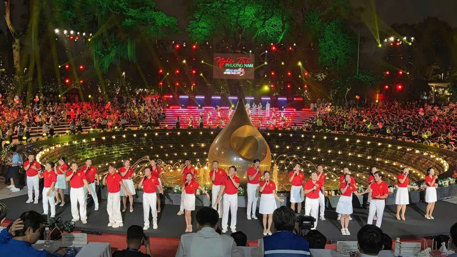 Nhóm nghệ sĩ mặc áo polo đỏ đồng phục chụp ảnh tại không gian sân khấu sự kiện.