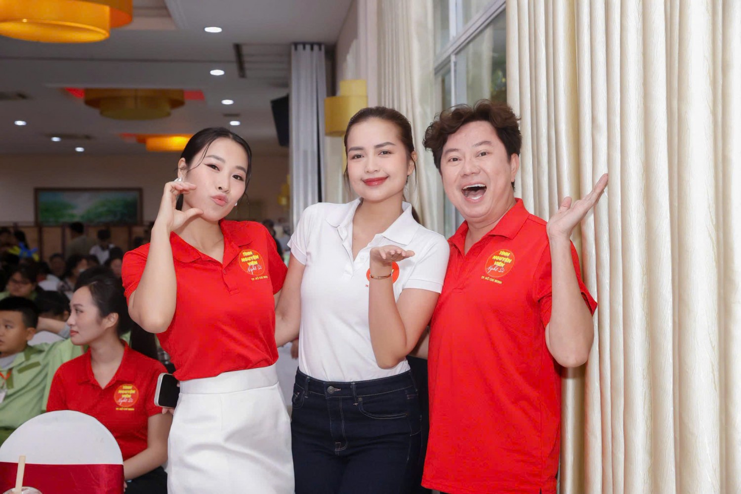 Hai người mặc áo polo đỏ tình nguyện viên nghệ sĩ chụp ảnh giao lưu cùng người tham dự.