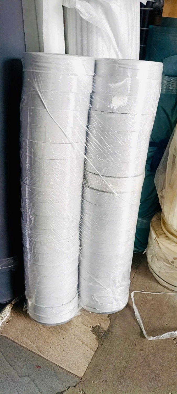 Cuộn vật liệu màu sáng được bọc bảo quản trong kho phụ liệu.