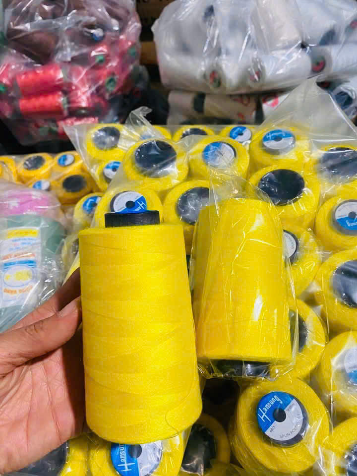 Nhân viên cầm cuộn chỉ vàng đối chiếu nguyên phụ liệu may đồng phục.