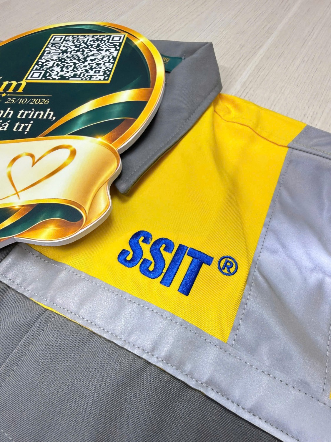 Logo SSIT màu xanh trên áo bảo hộ vàng xám có dải sáng.