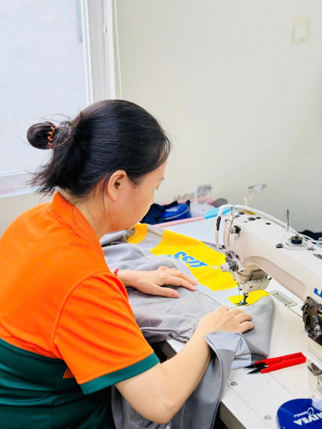 Người thợ Kim Vàng chăm chú may đường chỉ trên áo kỹ thuật SSIT vàng xám.