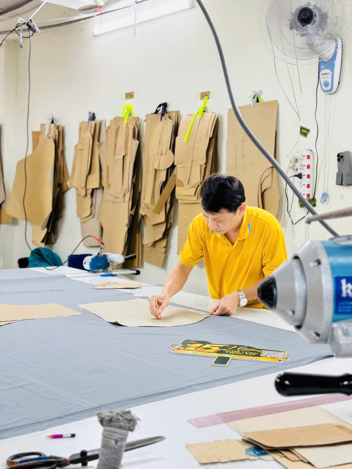 Người thợ Kim Vàng đặt rập giấy trên vải để chuẩn bị cắt chi tiết đồng phục.