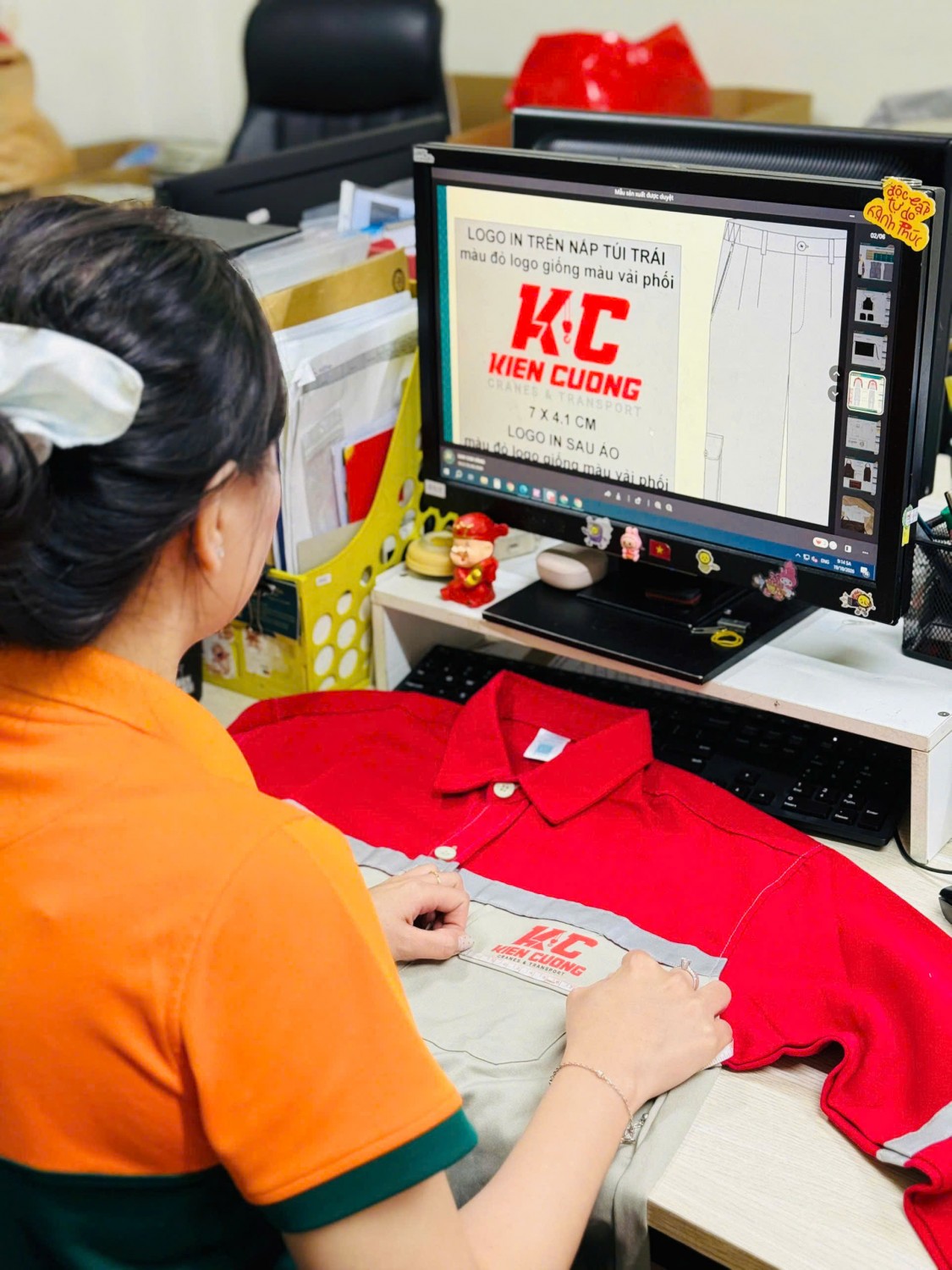 Nhân viên Kim Vàng đối chiếu áo bảo hộ Kiên Cường với bản thiết kế trên màn hình.